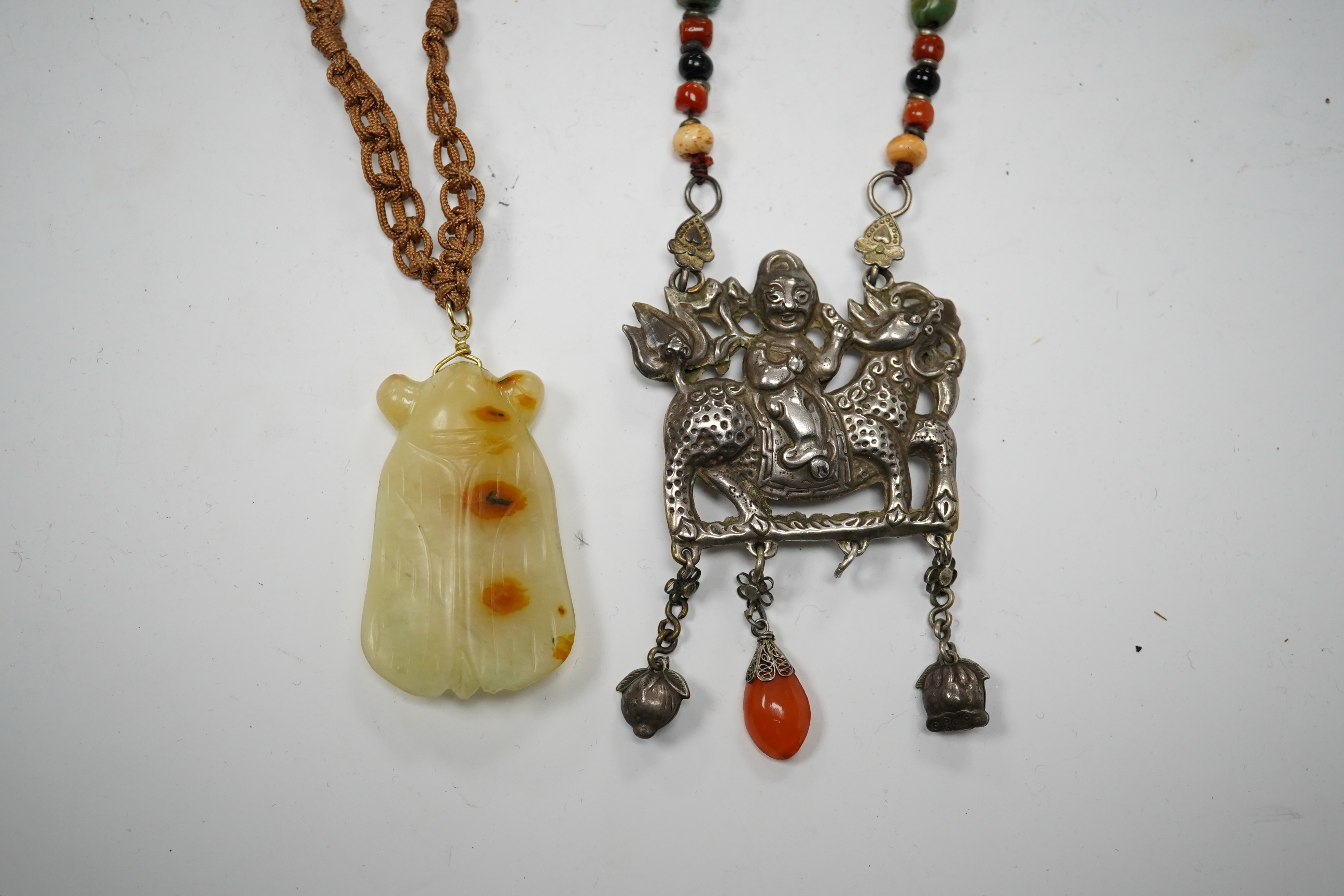 A Chinese celadon and russet jade cicada pendant on cording and a silver and stone mounted chain and pendant of boy riding a qilin, cicada 5.5cm long (2). Condition - tip of cicada wing chipped and on silver pendant one